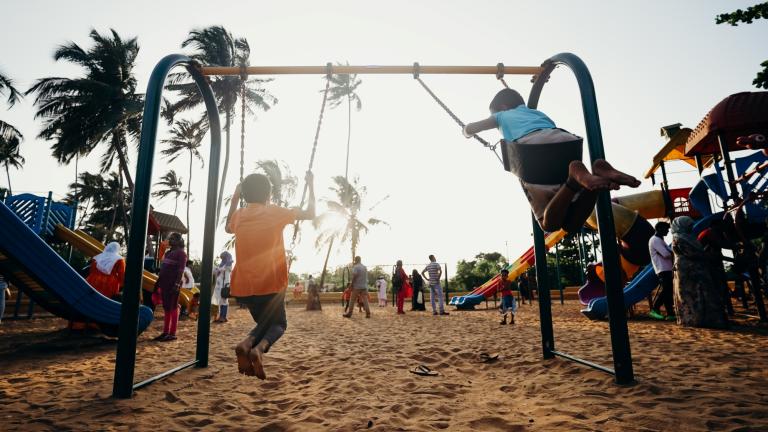 Anak-anak bermain ayunan di taman lingkungan yang dipenuhi pepohonan