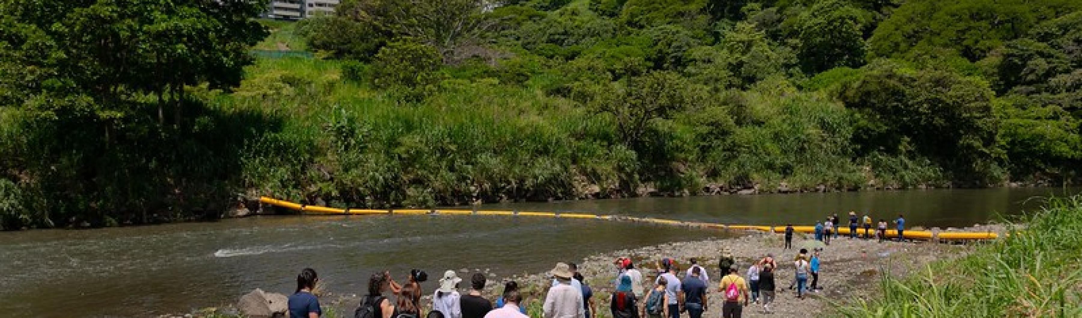 Para peserta Akademi Kota Kosta Rika berjalan menyusuri tepi Sungai Virilla untuk melihat penghalang plastik yang menjebak sampah.